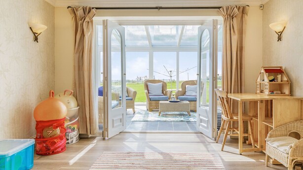 A spacious room with a large glass door leading to an outdoor seating area. - Penhallick House (Tintagel)