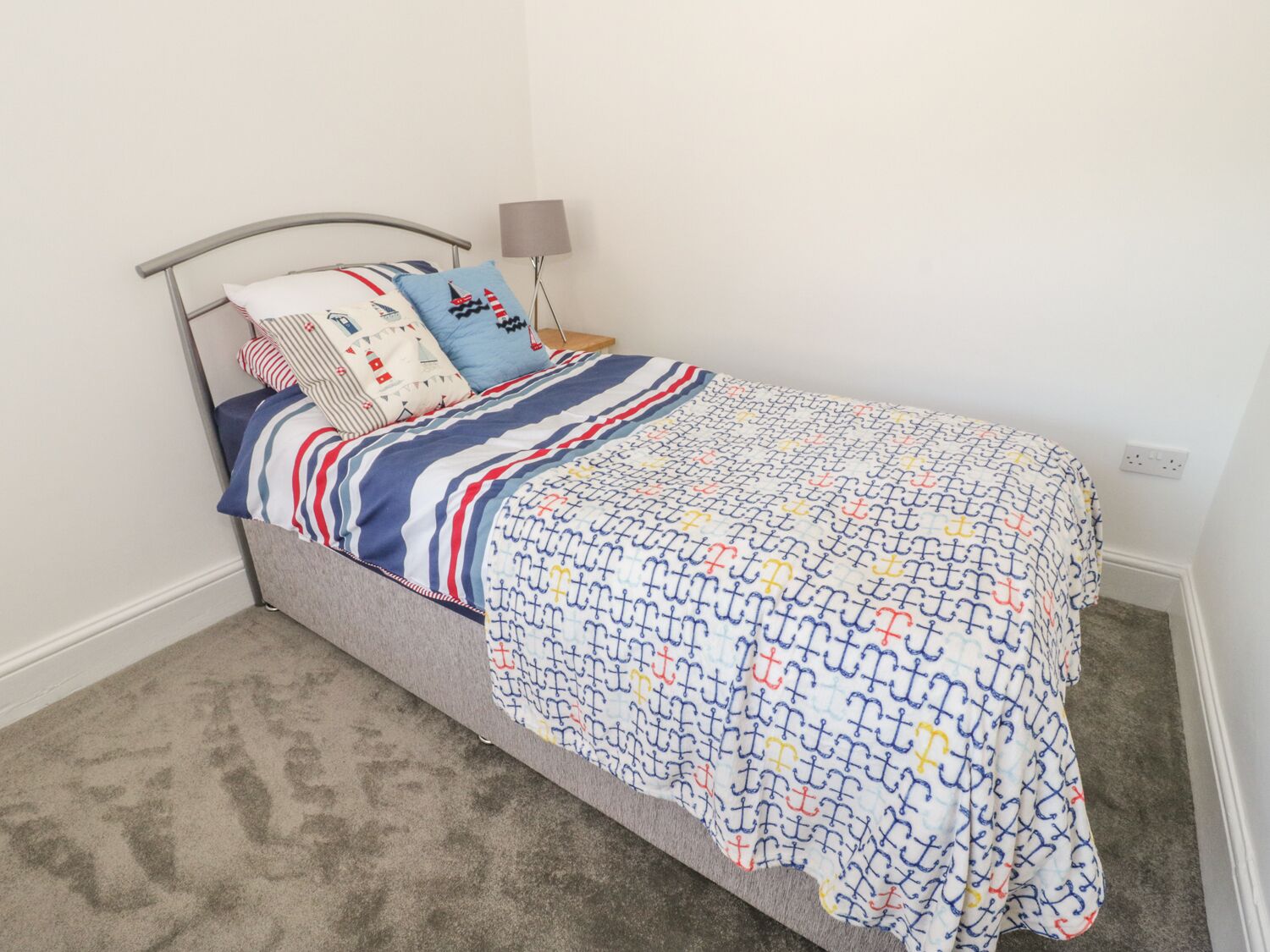 A single bed with a striped bedspread and multiple pillows in a room with a carpeted floor and a lamp.