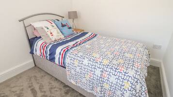 A single bed with a striped bedspread and multiple pillows in a room with a carpeted floor and a lamp.