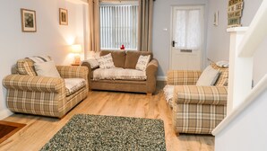 A cozy living room with a brown sofa set, a green patterned rug, and a blue pendant light.