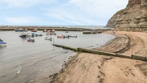 A coastal scene with boats docked at a pier, a sandy beach, and a cliff. - Bramla (Saltburn-by-the-Sea)