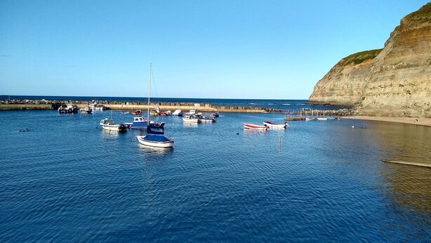 A coastal marina with several boats docked near a sandy beach and cliffs. - Bramla (Saltburn-by-the-Sea)