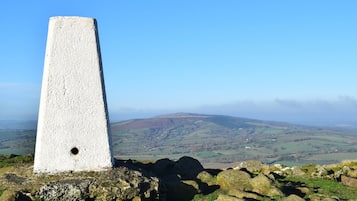A stone cairn on a rocky outcrop with a panoramic view of rolling hills and distant fields.