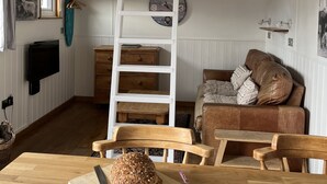 A cozy living room with a wooden table, a brown leather sofa, and a white ladder against the wall. - Shepherds Cabin at Titterstone Hot Tub &amp; Dog-friendly Near Ludlow (Ludlow)