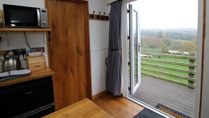 A kitchen with a microwave, kettle, and toaster, and a sliding glass door leading to a balcony with a view of a green landscape and sheep. - Shepherds Cabin at Titterstone Hot Tub &amp; Dog-friendly Near Ludlow (Ludlow)