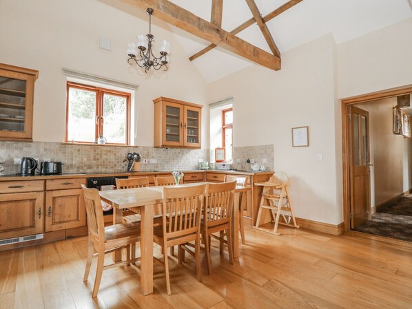 A spacious kitchen with wooden cabinets, a dining table, and chairs. - The Cottage (Watchet)
