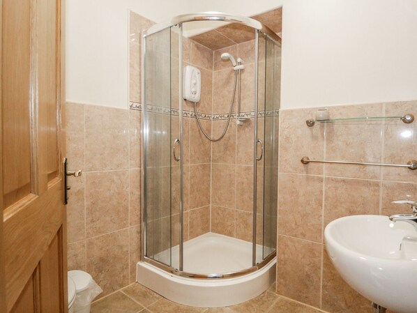 A shower enclosure with a glass door, a handheld showerhead, and a handheld shower nozzle. - The Cottage (Watchet)