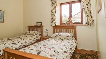 A bedroom with two single beds, a window with curtains, a bedside lamp, and a teddy bear on one bed.