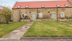 A stone building with a red-tiled roof, two doors, and a small garden area with a pathway. - Cross Cottage (Durham)