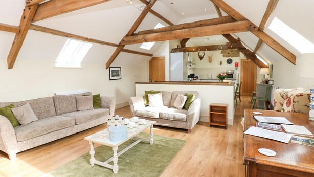 A spacious loft with high ceilings, exposed wooden beams, a cozy living area with a sofa and coffee table, and a kitchen in the background. - Cross Cottage (Durham)