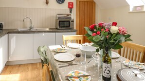 A dining area with a table set for four, a microwave, and a clock on the wall. - Cross Cottage (Durham)