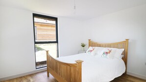 Ein Schlafzimmer mit einem hölzernen Bett, weißer Bettwäsche und einem Fenster mit Blick auf eine Holzkonstruktion draußen.