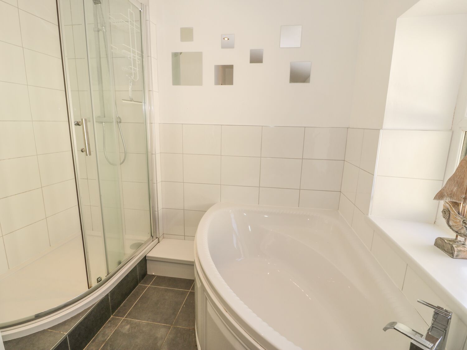 A modern bathroom with a glass shower enclosure, a freestanding bathtub, and a tiled wall with recessed lighting.