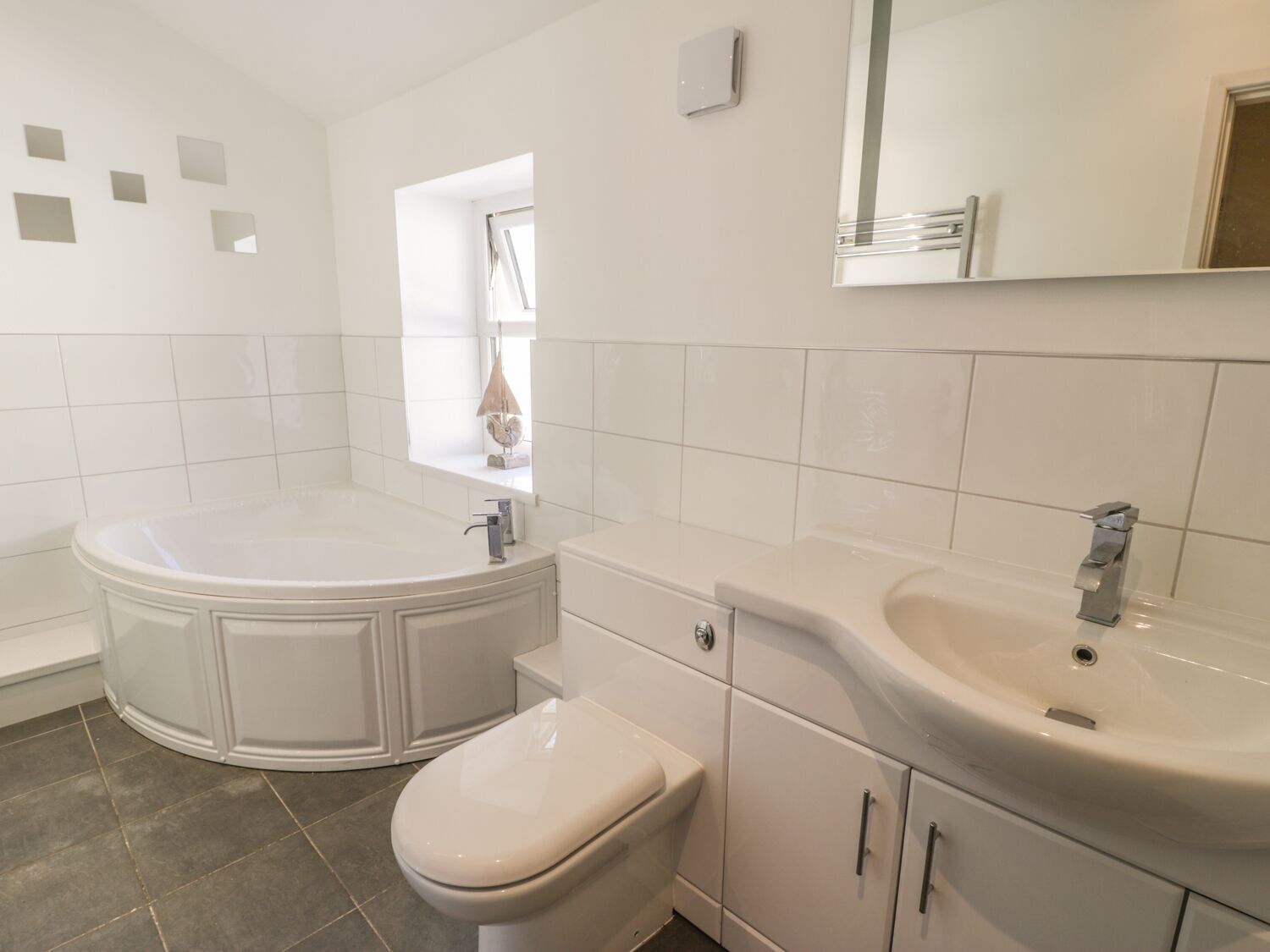 A bathroom with a bathtub, toilet, and sink, featuring white tiles and a window with a view.