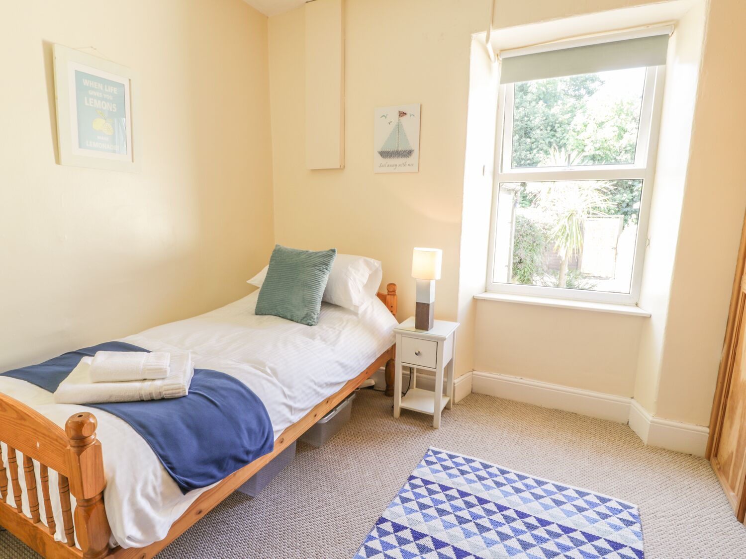 Een slaapkamer met een bed, een nachtkastje met een lamp, een raam en een vloerkleed.