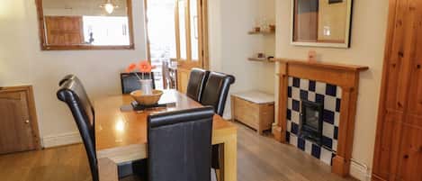 A dining area with a wooden table, black leather chairs, a vase with flowers, and a checkered fireplace.