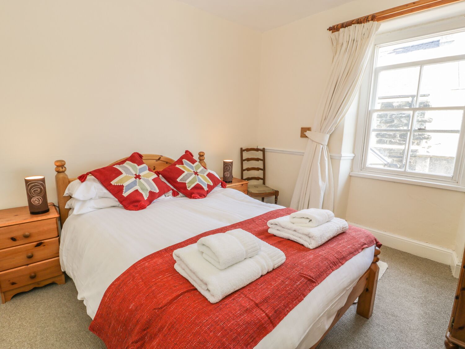 A neatly made bed with a red and white bedspread, two decorative pillows, and folded towels on the side.