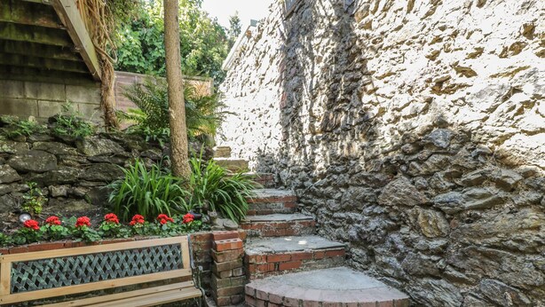Un muro de piedra con un banco de madera y una maceta con flores rojas.