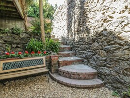 Un muro de piedra con un banco de madera y una maceta con flores rojas.