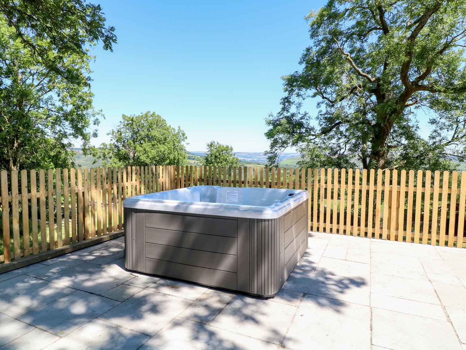A hot tub on a patio with a wooden fence and trees in the background.