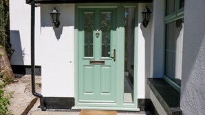A white building with a green door, two black wall-mounted lamps, and a small window above the door. - Ty Ffarm at Gellilwch (Pontypridd)
