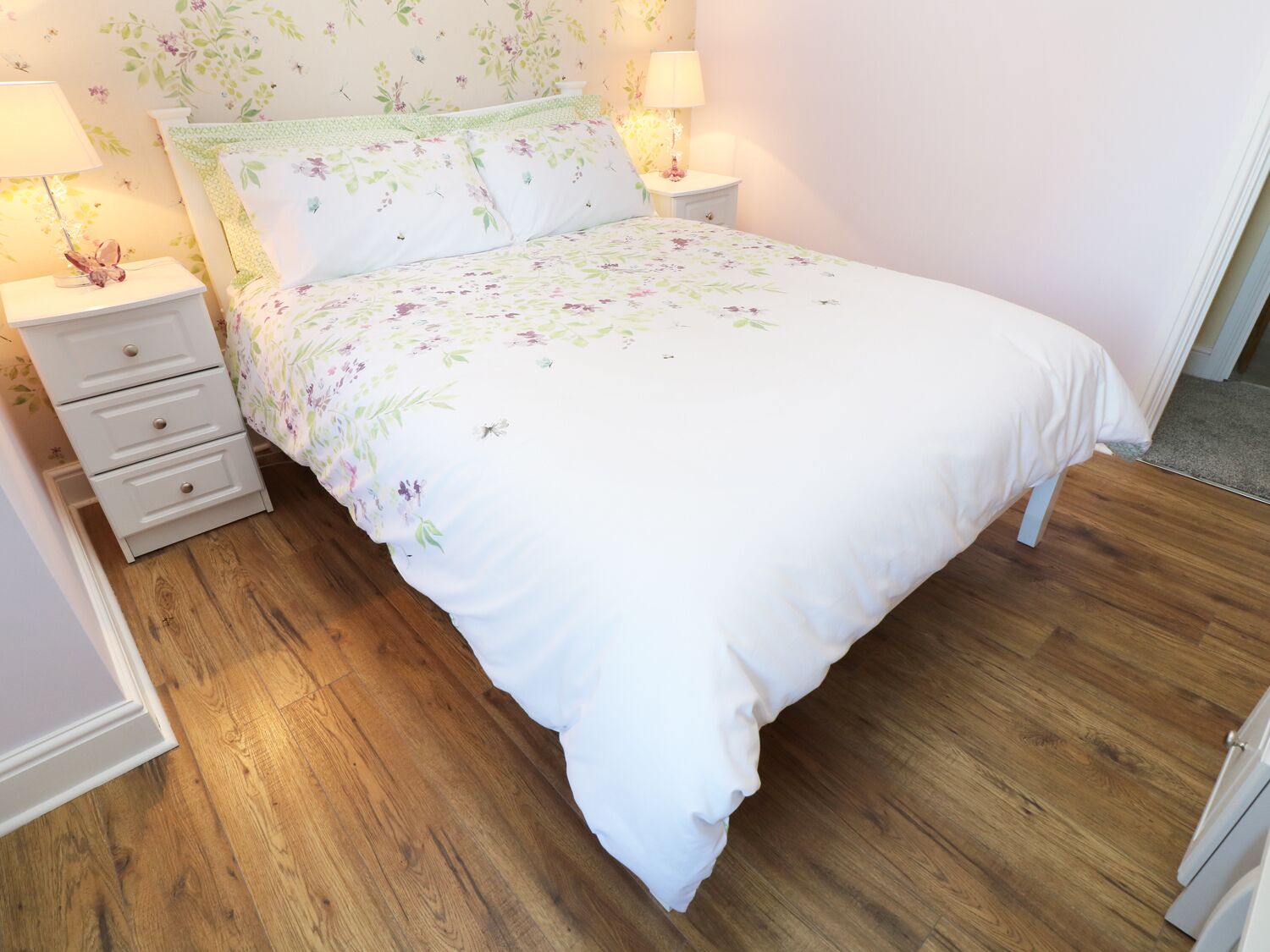 A bedroom with a floral bedspread, a bedside table with a lamp, and a nightstand with a lamp.