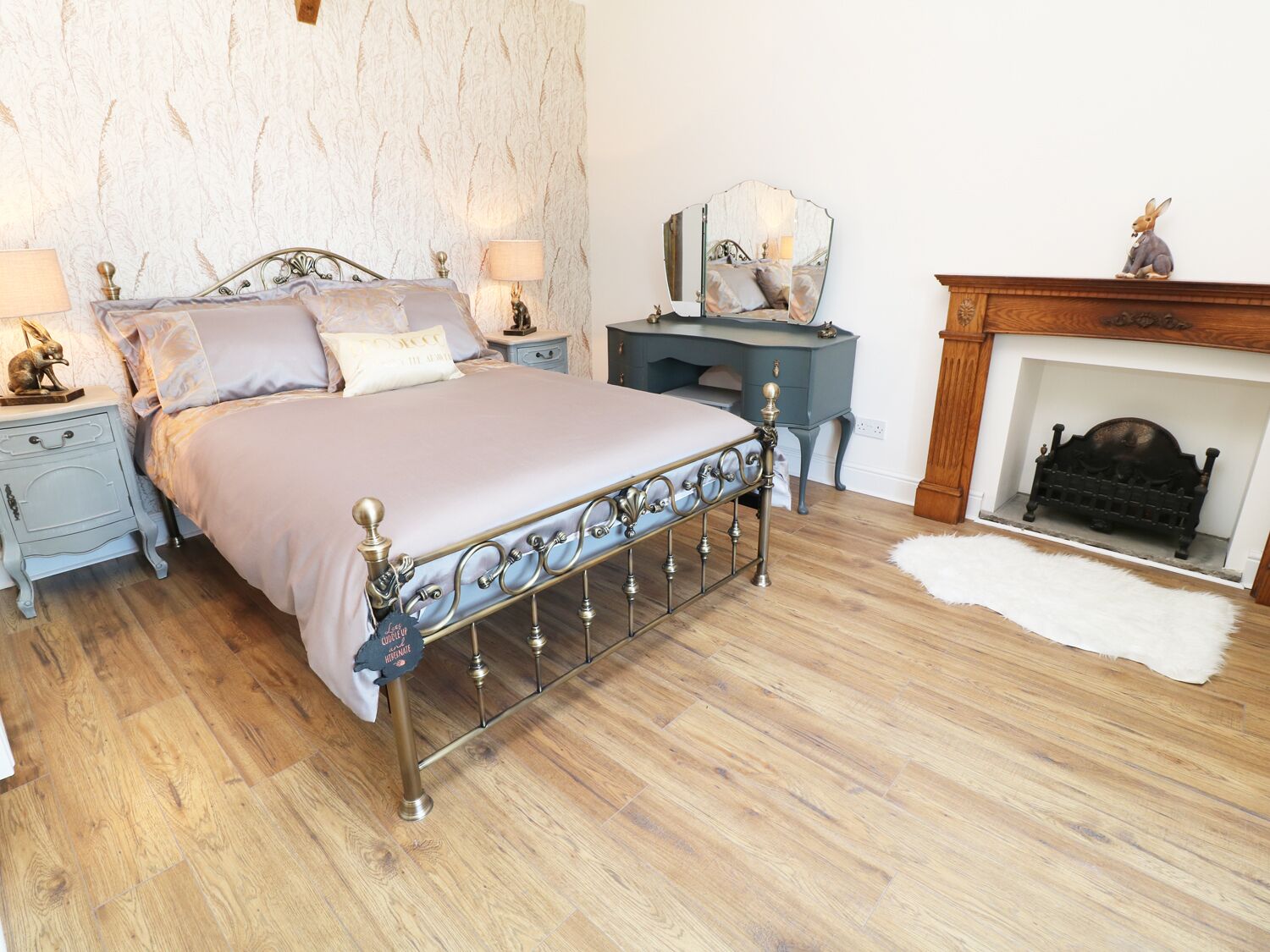 A bedroom with a metal-framed bed, a nightstand with a lamp, a dresser, a mirror, and a fireplace.