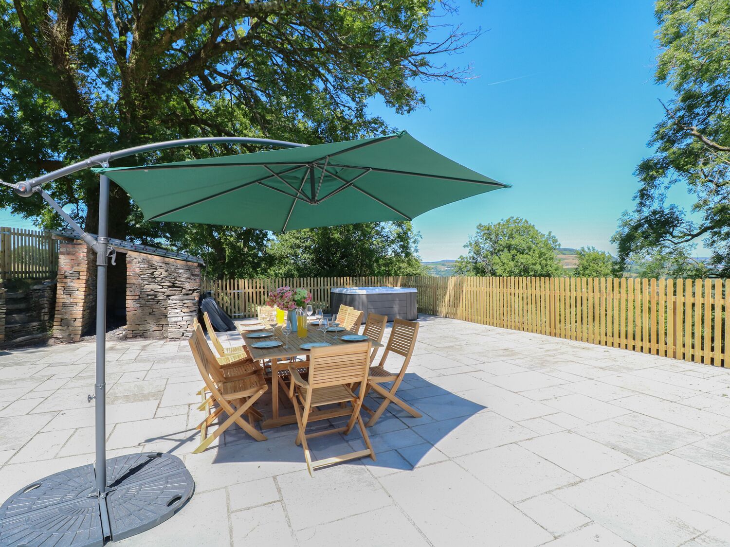 An outdoor patio with a table and chairs, a green umbrella, and a stone wall.