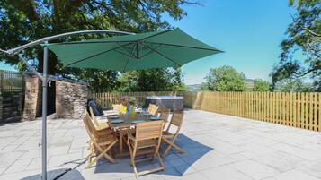 An outdoor patio with a table and chairs, a green umbrella, and a stone wall.