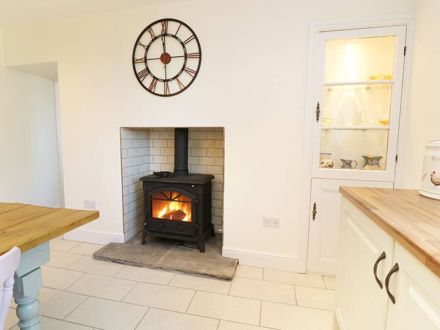 A kitchen with a wood-burning stove, a clock on the wall, and a cabinet with a glass door.