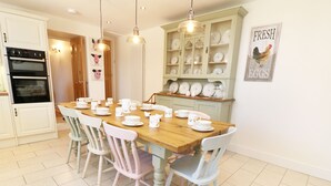 A dining area with a wooden table set for four, surrounded by white chairs. - Ty Ffarm at Gellilwch (Pontypridd)
