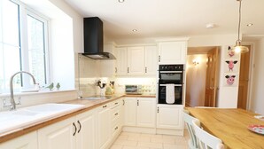 A modern kitchen with white cabinets, a wooden countertop, a built-in oven, and a window providing natural light. - Ty Ffarm at Gellilwch (Pontypridd)