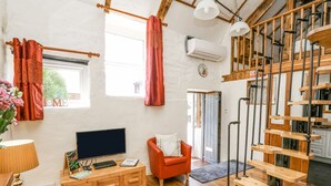 A cozy living room with a wooden TV stand, a red sofa, and a staircase with wooden steps. - Rose Cottage (Llandysul)
