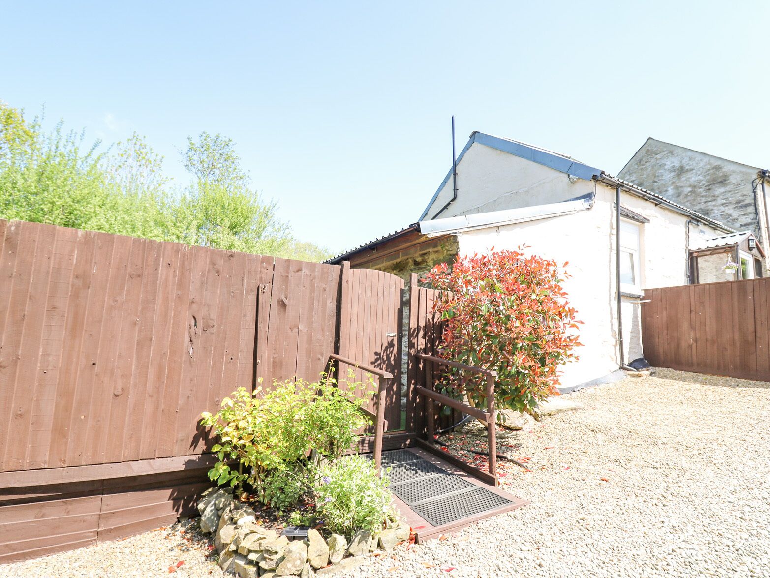 A residential property with a gravel driveway, a wooden fence, and a small garden with a variety of plants.