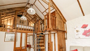 A wooden staircase with a metal railing leading to an upper floor, a white wall with a floral painting, and a beige sofa with red cushions. - Rose Cottage (Llandysul)