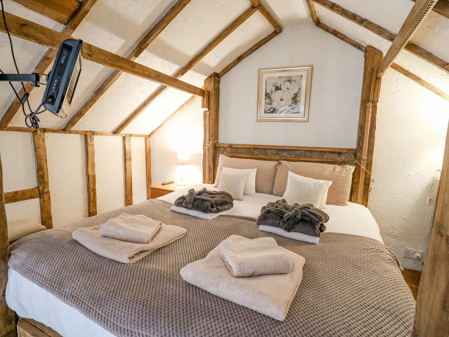 A cozy bedroom with a sloped ceiling, a bed with multiple pillows, a bedside table with a lamp, and a framed picture on the wall.