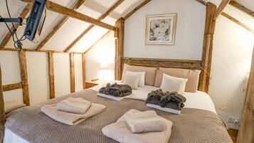 A cozy bedroom with a sloped ceiling, a bed with multiple pillows, a bedside table with a lamp, and a framed picture on the wall.