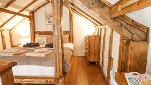 A cozy attic bedroom with a wooden bed, a dresser, and a small table with towels and a box of chocolates. - Rose Cottage (Llandysul)