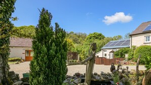 A rustic garden with a wooden sculpture, a pond, and a stone wall. - Rose Cottage (Llandysul)