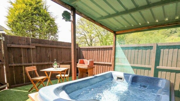 A hot tub with a control panel, surrounded by a wooden deck and a covered patio area. - Rose Cottage (Llandysul)