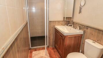 A bathroom with a shower, sink, toilet, and wooden paneling.