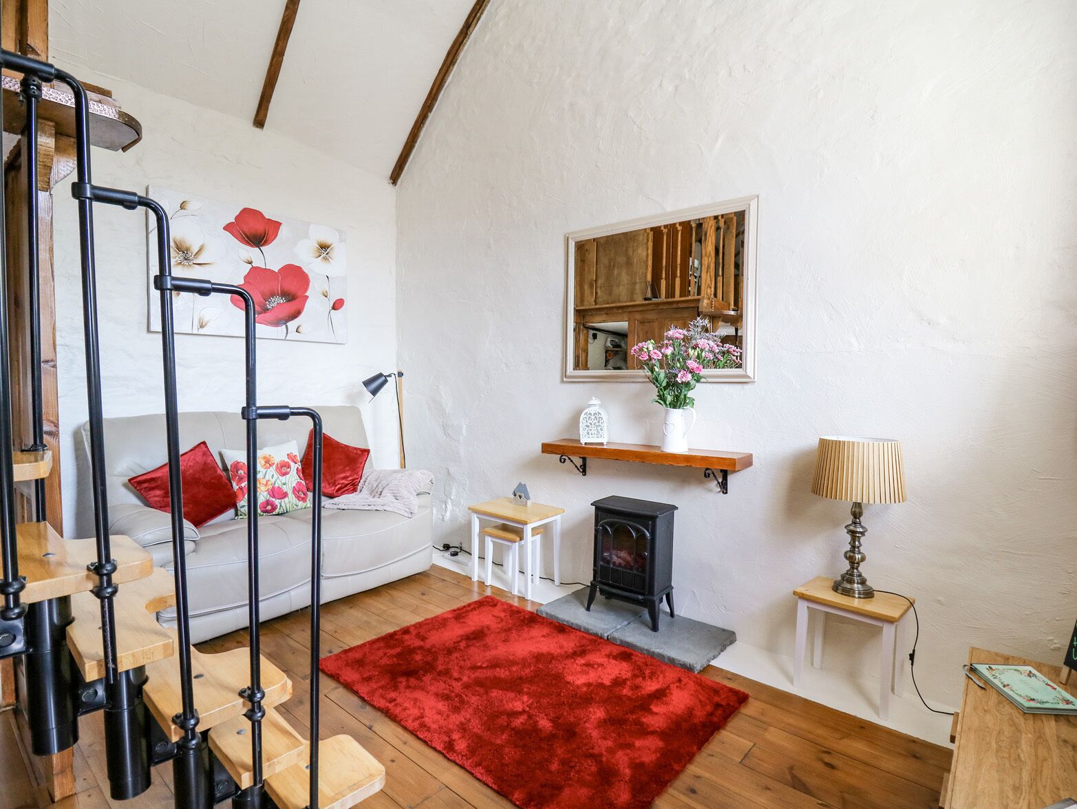 Una sala de estar acogedora con una escalera, un sofá, una alfombra roja, una chimenea y un espejo en la pared.