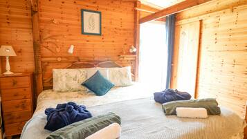 A wooden cabin room with a bed, a nightstand, a framed leaf artwork, and a window.