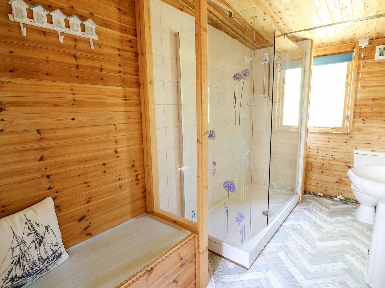 Interior de una cabaña de madera con ducha envuelta en vidrio, un banco de madera y un inodoro.