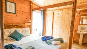 Habitació de cabana de fusta amb un llit, almoades, una finestra i un bany amb un rentapeus.