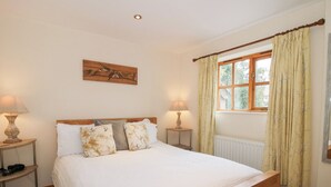 A bedroom with a wooden bed, two bedside tables with lamps, a window with curtains, and a wall-mounted artwork of birds. - Old Hall Barn 1 (Church Stretton)