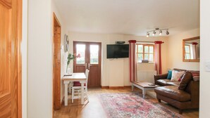 A cozy living room with a wooden floor, a brown leather sofa, a white table, and a TV mounted on the wall. - Old Hall Barn 1 (Church Stretton)