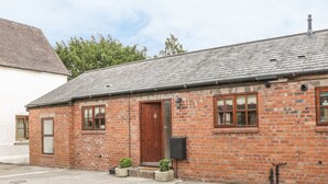 A brick building with a wooden door, windows, and a small garden area with potted plants. - Old Hall Barn 1 (Church Stretton)