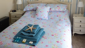 Una cama bien hecha con ropa de cama floral, una decoración de estrella de mar, toallas dobladas y artículos de aseo en una mesita de noche.