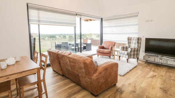 A spacious living area with a sofa, chairs, a dining table, and a TV. - Swan Lodge Castle Farm (Wedmore)